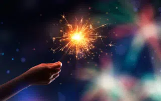 Hand holding a burning sparkler against fireworks background