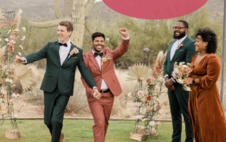 two-men-smiling-in-tuxedos-walking-down-the-aisle-together-outside-from-their-wedding